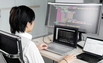 A software developer working on code with multiple screens in a modern office setting.